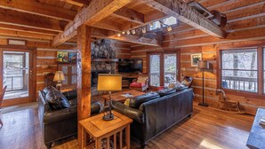 A log cabin interior with a fireplace, leather sofas, a dining table, and large windows. - Daniel Boone Lodge (Boone)