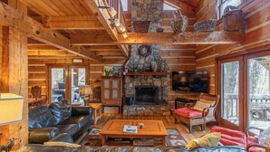 A log cabin interior with a stone fireplace, leather furniture, and a television. - Daniel Boone Lodge (Boone)