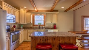 A kitchen with wooden beams, a granite countertop, stainless steel appliances, and wooden bar stools. - Skyland Cabin (Boone)