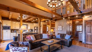 A spacious living area with a large wooden ceiling, a kitchen in the background, and a cozy seating arrangement. - Gratitude (Blowing Rock)