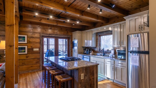 A kitchen with wooden beams, white cabinets, stainless steel appliances, and a bar area with stools. - Gratitude (Blowing Rock)
