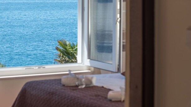 A room with a view of the sea, a bed with a blanket, and a window with a curtain. - Apartment Villa Daniela (Okrug)