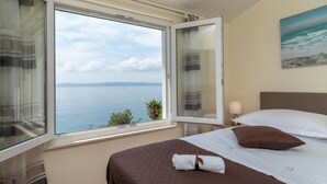 Un dormitorio con un amplio ventanal que ofrece vistas al mar. La habitación tiene una cama con cubrecama marrón y almohadas blancas.