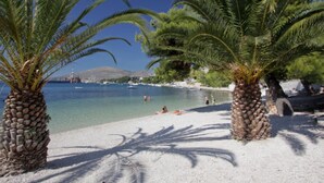 A beach with palm trees, clear water, and boats in the distance. - Apartment Villa Daniela (Okrug)