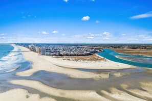 Un complejo turístico costero con propiedades frente a la playa, un muelle que se adentra en el mar y un cielo despejado.
