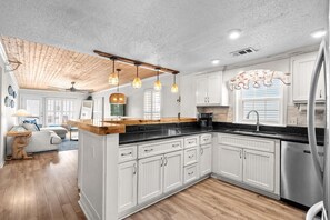 Uma cozinha moderna com armários brancos, bancada de madeira e iluminação pendente.
