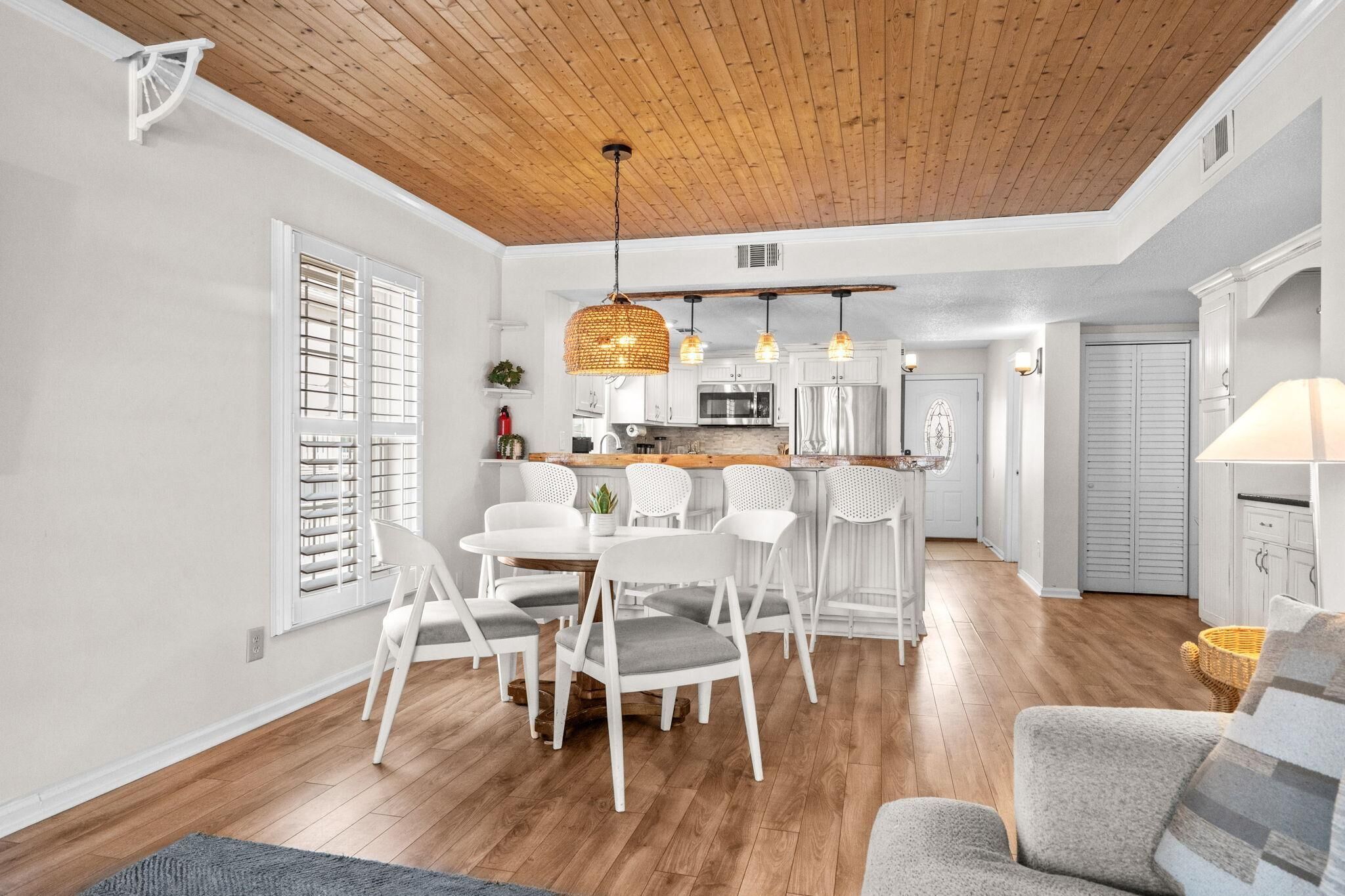 A spacious kitchen with wooden flooring, white cabinetry, and a dining area with white chairs.