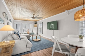 A modern living room with a ceiling fan, a TV mounted on the wall, and a dining area with a table and chairs.