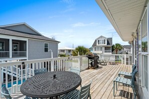 A wooden deck with a round table and chairs, a barbecue grill, and a pool in the background.