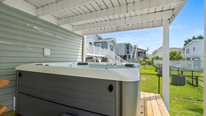 A hot tub under a covered patio with a view of houses in the background. - Grove Cove | Beach 2 Min | Dog-Friendly | Hot Tub (North Myrtle Beach)