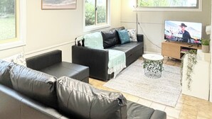 A modern living room with a leather sofa, a black couch, a coffee table, and a flat-screen TV mounted on a wooden stand. - Buller Street Home (Charlestown)