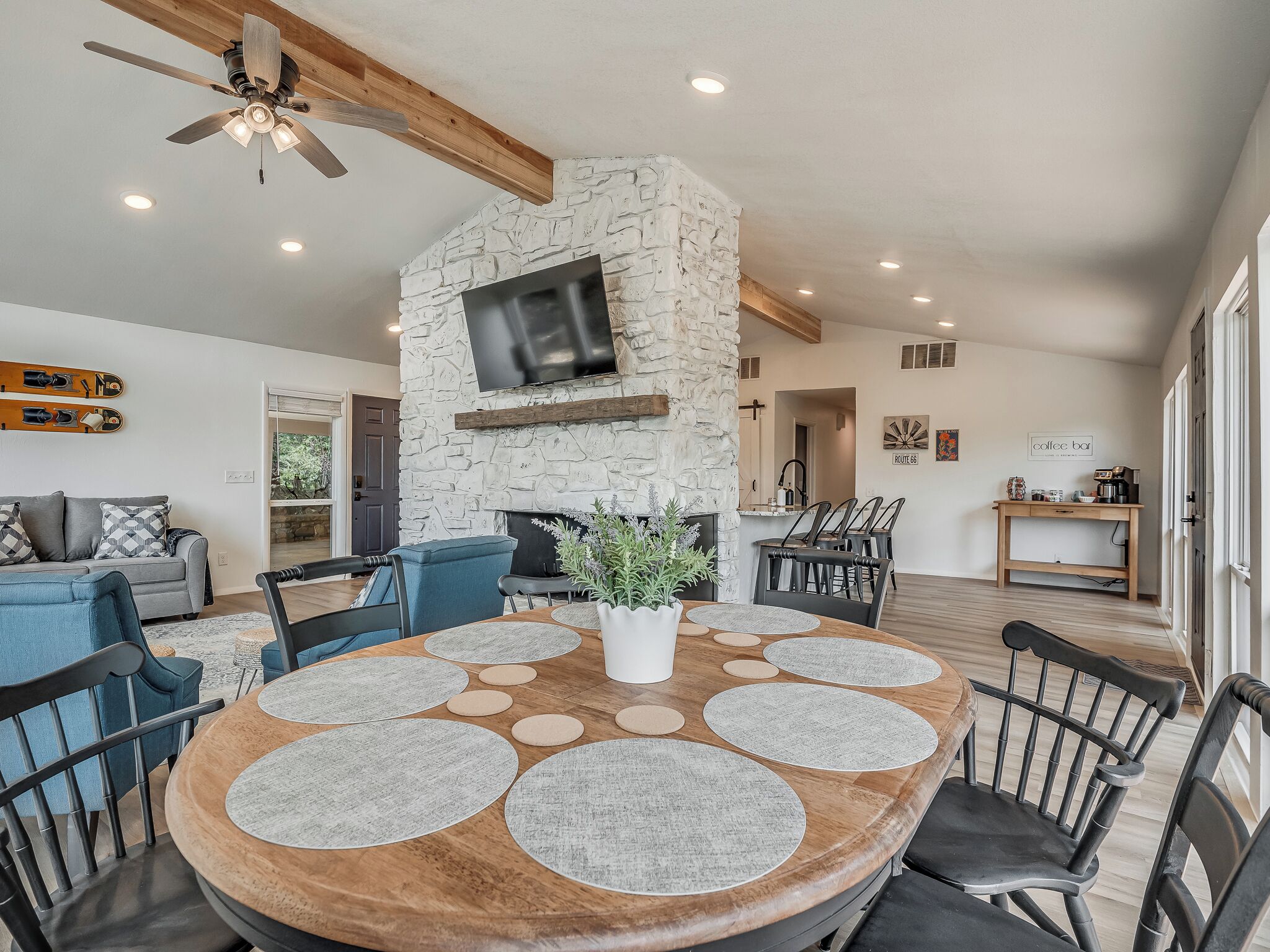 Un salon moderne doté d’une cheminée en pierre, d’un ventilateur de plafond et d’un coin repas avec une table ronde et des chaises.