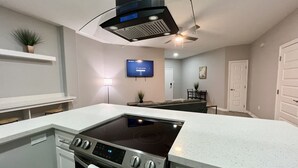 A modern kitchen with a built-in stove, a ceiling fan, and a flat-screen TV mounted on the wall. - Villa Escondida #2 -2BD- Straight Shot to SpaceX! (Brownsville)