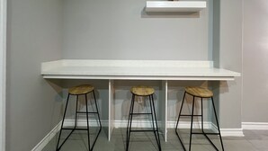 A kitchen with a white countertop, three wooden stools, and two wall-mounted shelves with plants. - Villa Escondida #2 -2BD- Straight Shot to SpaceX! (Brownsville)