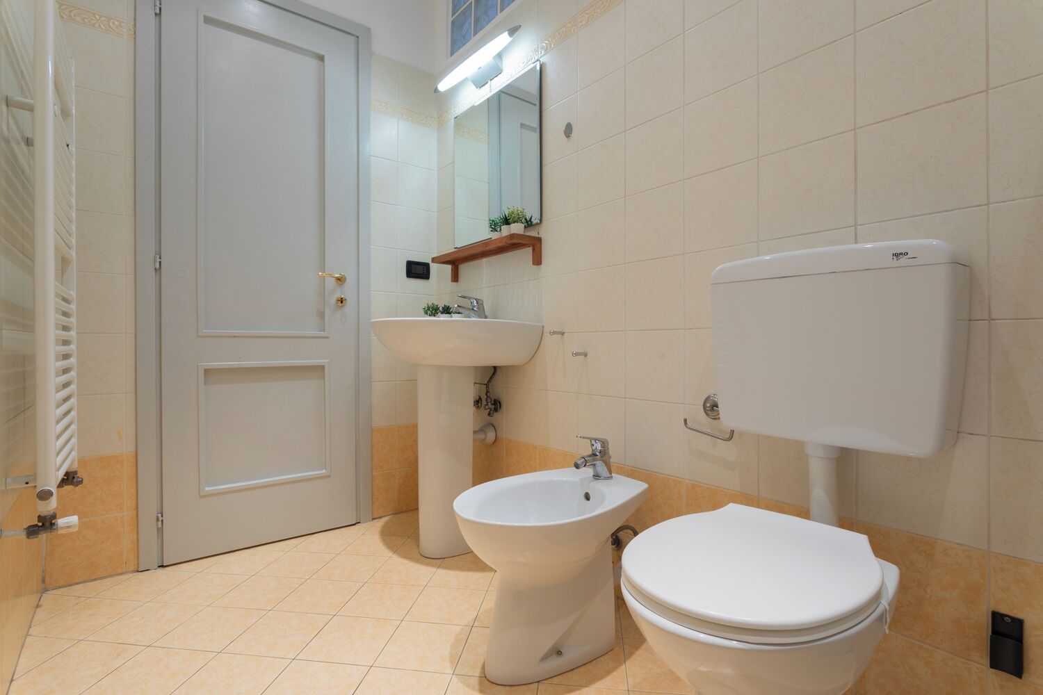 A bathroom with a toilet, bidet, sink, and a mirror above the sink.