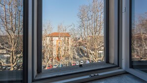 A window with a view of a building with a red roof and multiple windows, surrounded by bare trees and parked cars. - Light Blue Apartment by Wonderful Italy (Turin)