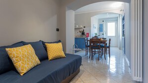 A living room with a sofa and two yellow pillows, a dining area with a table and chairs, and a kitchen in the background. - Light Blue Apartment by Wonderful Italy (Turin)
