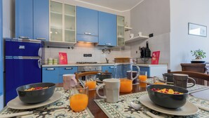 A modern kitchen with blue cabinets, a refrigerator, a dining table set with breakfast items, and a coffee machine. - Light Blue Apartment by Wonderful Italy (Turin)