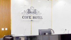 Un mostrador de recepción con una pared de mármol que muestra el logotipo y el nombre de CAFE HOTEL.