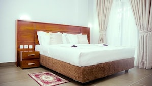 Una habitación de hotel con una cama grande, cabecera de madera, mesitas de noche y una alfombra estampada en rojo y blanco.
