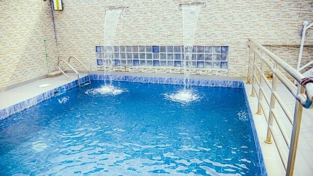 Una piscina interior con agua cristalina, pared de azulejos y barandilla de metal.