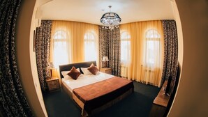Une chambre d’hôtel avec un grand lit, deux tables de chevet, une commode et un lustre.