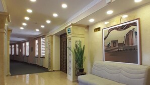 Un hall d’hôtel avec un comptoir d’accueil, un canapé, une plante en pot et un grand tableau encadré au mur.