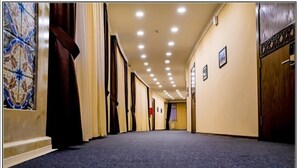 Un couloir d’hôtel avec un sol recouvert de moquette, des carreaux muraux décorés et une rangée de portes d’un côté.