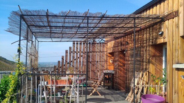 Un bâtiment en bois doté d’un espace extérieur couvert, de murs en pierre et de divers pots de plantes.