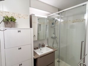 Bathroom features a glass-enclosed shower, a cabinet with multiple drawers, and a decorative tile border.