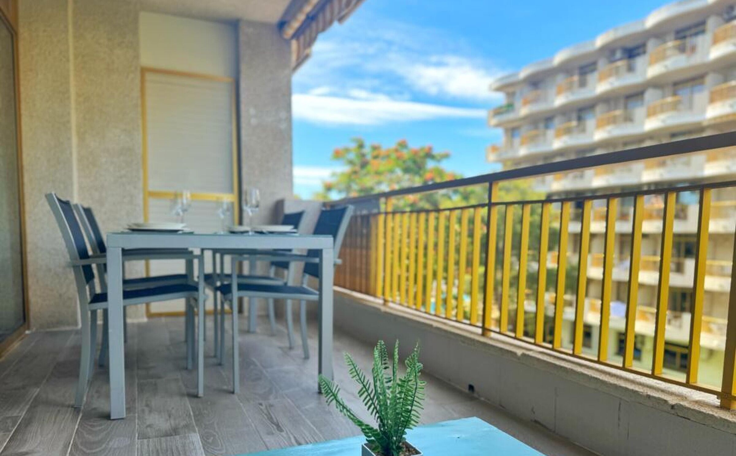 A balcony with a table and chairs, a potted plant, and a view of a building with balconies.