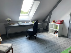 A modern loft bedroom with a sloped ceiling, a skylight, a desk, a chair, a bookshelf, and a small trash can.