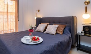 Un dormitorio con cama, mesita de noche, lámpara y una bandeja con fresas y una taza.