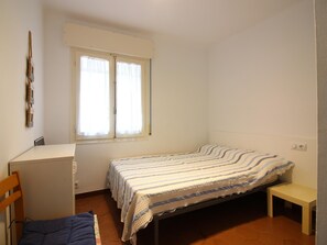 A small, simple room with a bed, a desk, and a chair.