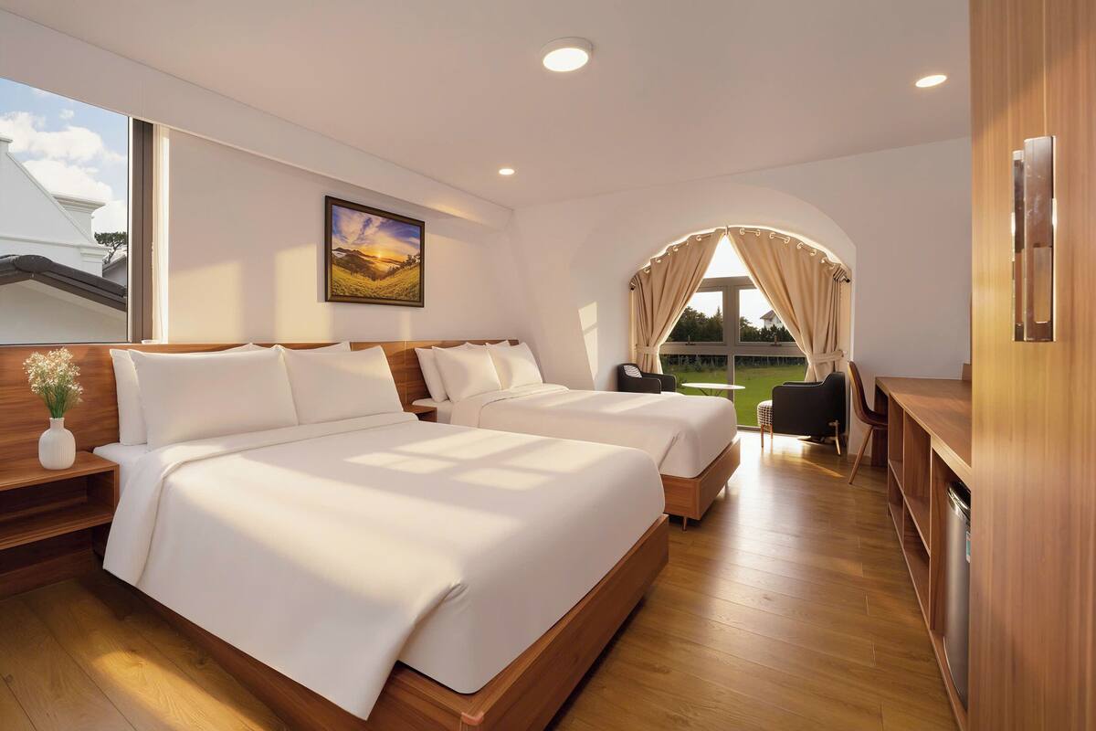 A modern hotel room with two beds, a wooden floor, a large window, and a view of the outdoors.