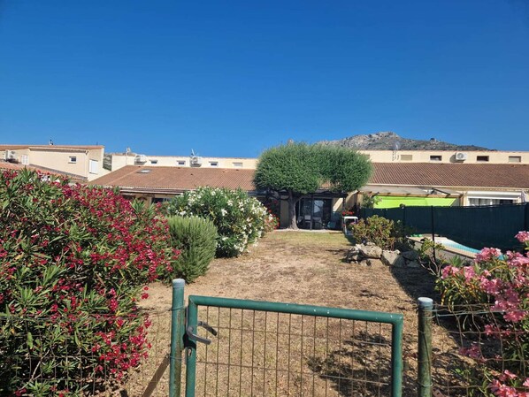 A courtyard with a small seating area, a fenced garden with various plants, and buildings in the background.
