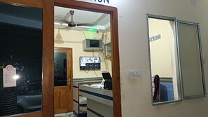 Una habitación con puerta de madera, ventilador de techo, televisor montado en la pared y un espejo con un letrero encima.