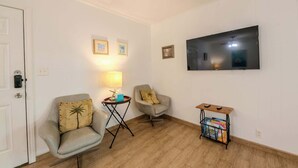 Una habitación con dos sillones, una mesita con una lámpara, un televisor en la pared y una mesita auxiliar con revistas.
