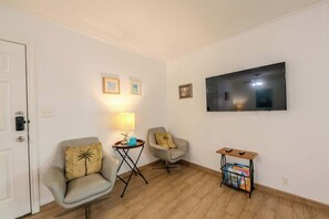 Una habitación con dos sillones, una mesita con una lámpara, un televisor en la pared y una mesita auxiliar con revistas.