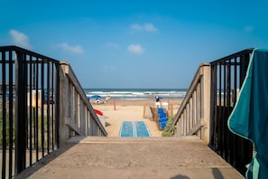 Een strand met houten trappen die naar het zand leiden, een uitkijktoren van de strandwacht en een helder uitzicht op de oceaan.