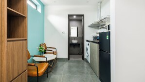 A compact kitchen with a washing machine, a sink, and a refrigerator. There is a dining area with chairs and a table, and a wooden cabinet. - Saluton Apartment (Da Nang)