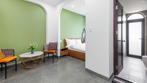 A modern hotel room with a green accent wall, a wooden bed, a small table with a vase, and a chair. - Saluton Apartment (Da Nang)