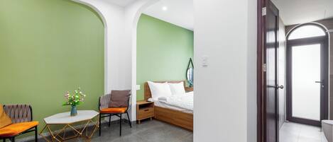 A modern hotel room with a green accent wall, a wooden bed, a small table with a vase, and a chair.
