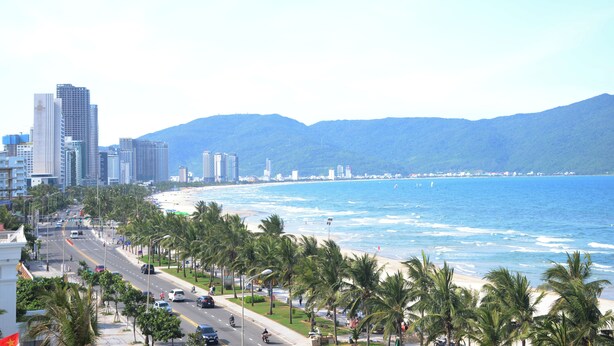 A coastal cityscape with a beach, palm trees, and high-rise buildings. - Saluton Apartment (Da Nang)