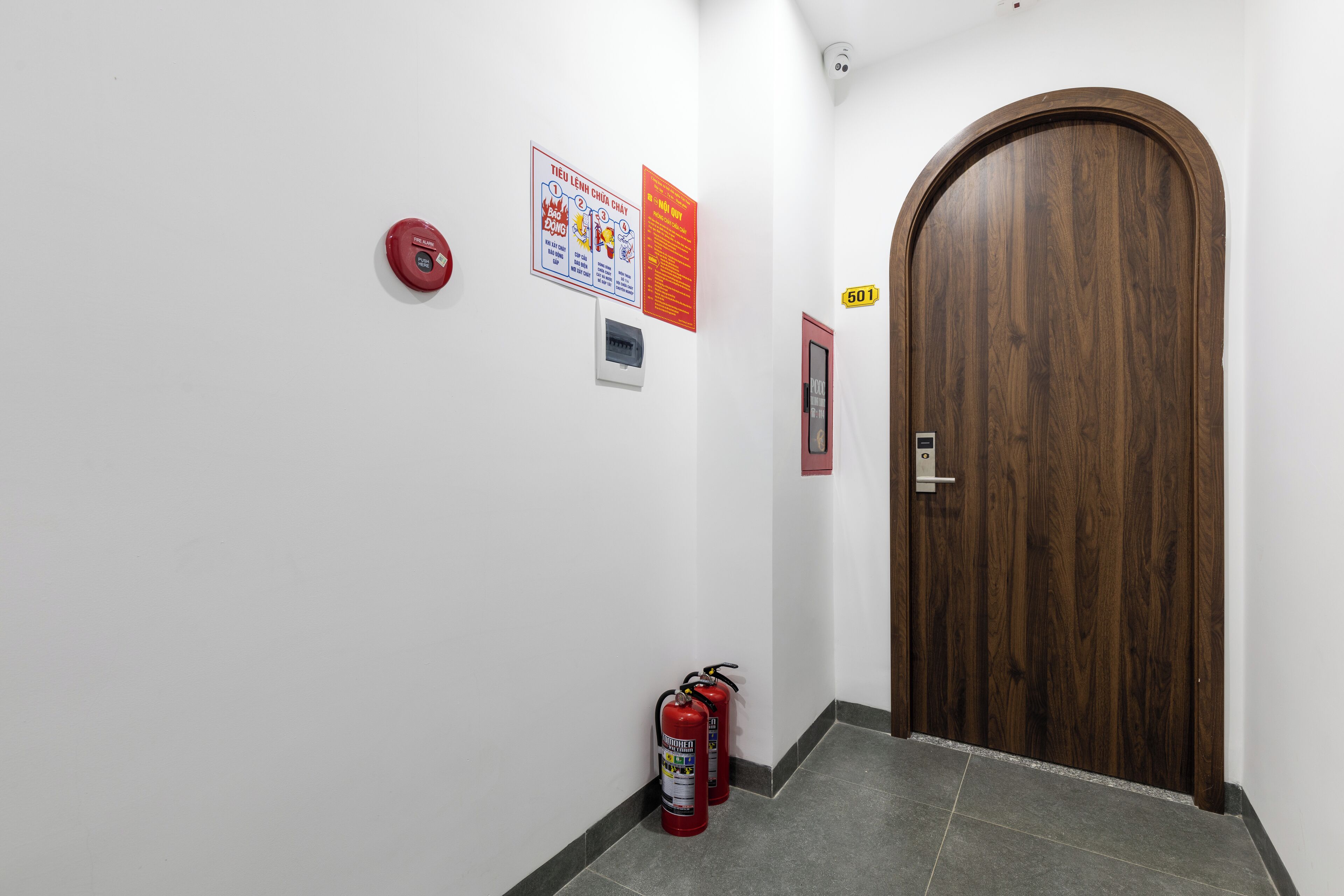 A hallway with a wooden door, fire extinguishers, and informational posters on the wall.