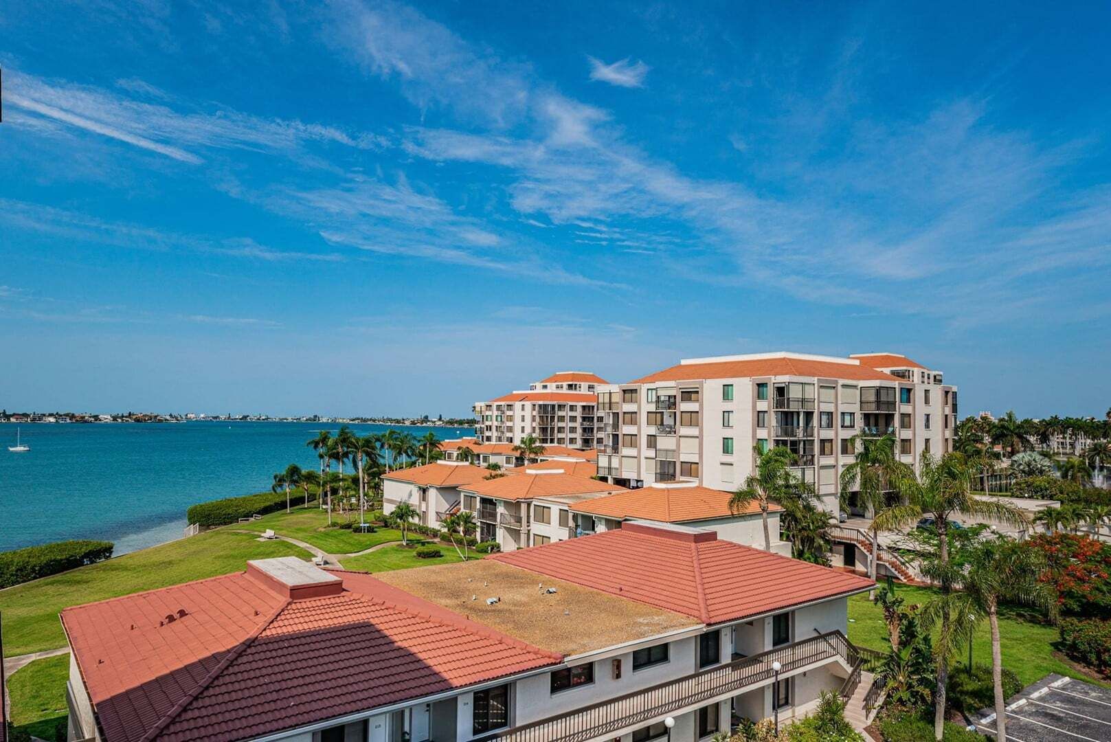 Un hotel con varias construcciones, techo de tejas rojas y vista al mar.