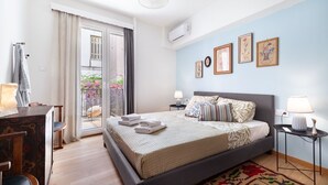 A bedroom with a bed, bedside tables, a dresser, a window with curtains, and a balcony with plants. - Athenian Gate To Plaka (Athens)
