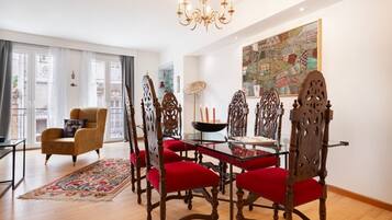 Un comedor con una mesa de vidrio y sillas ornamentadas, una araña y un cuadro abstracto grande en la pared.