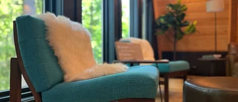 A teal upholstered chair with a white fluffy pillow, positioned in a room with wooden walls and large windows.