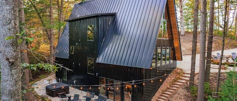 Uma cabana moderna com telhado inclinado, grandes janelas e um terraço com área de estar ao ar livre.